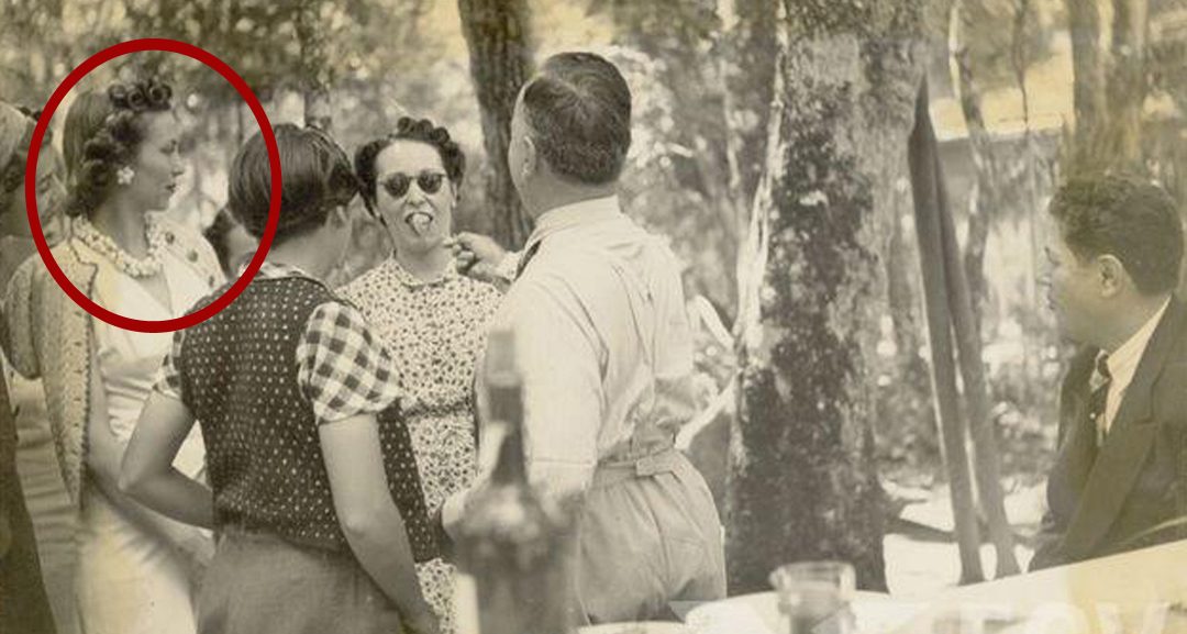 Photographie ancienne d’une réception en plein air : Aimée Sotto Mayor, entourée d’un cercle rouge, converse avec un groupe d’invités