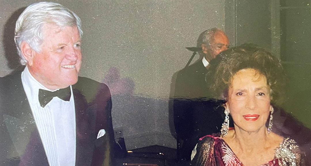 Photographie en couleur d’une soirée : Ted Kennedy en smoking et Aimée de Heeren en robe du soir, un pianiste à l’arrière-plan